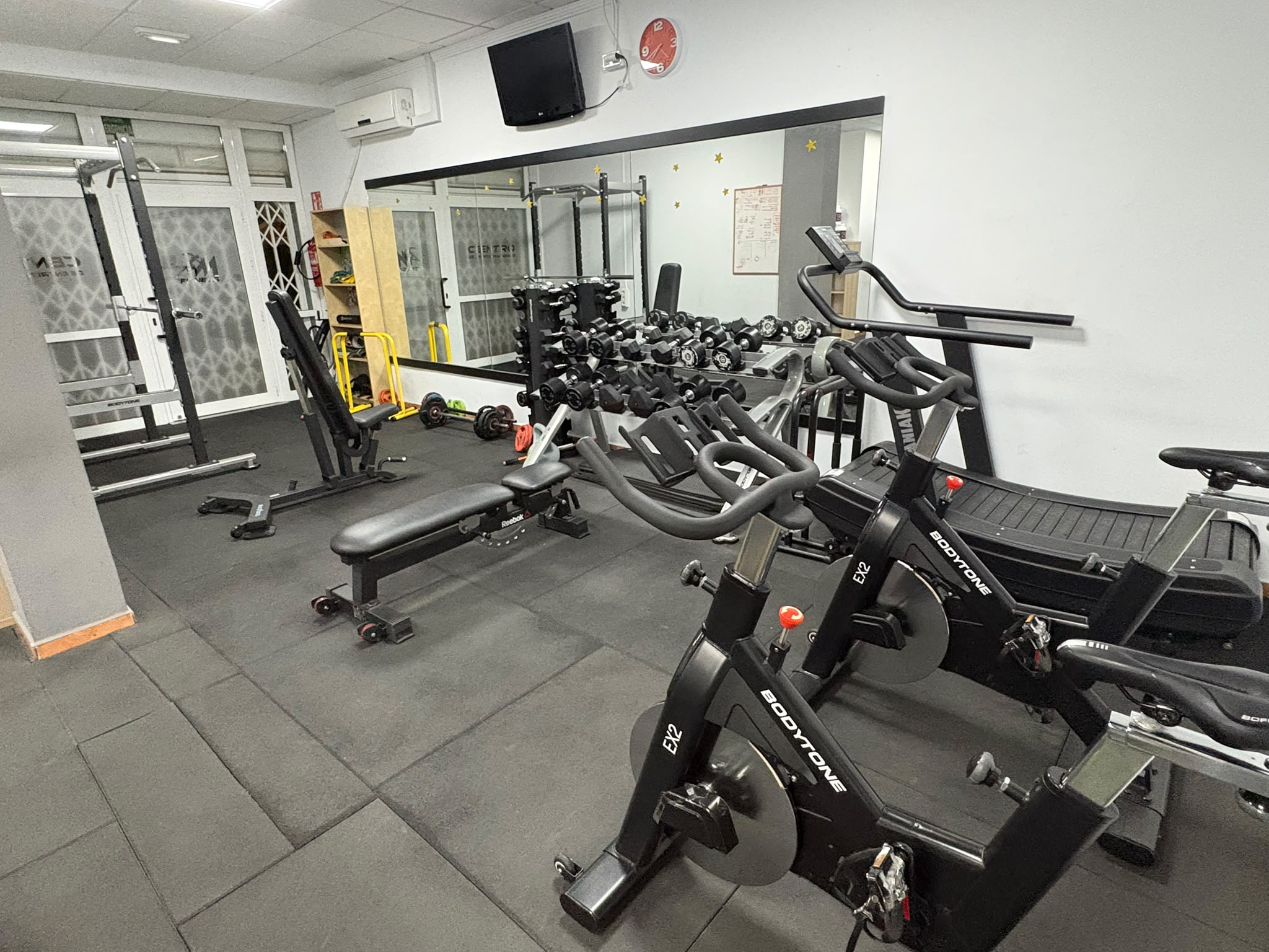 Bicicletas de spinning, cinta curva y mancuernas en la entrada del gimnasio